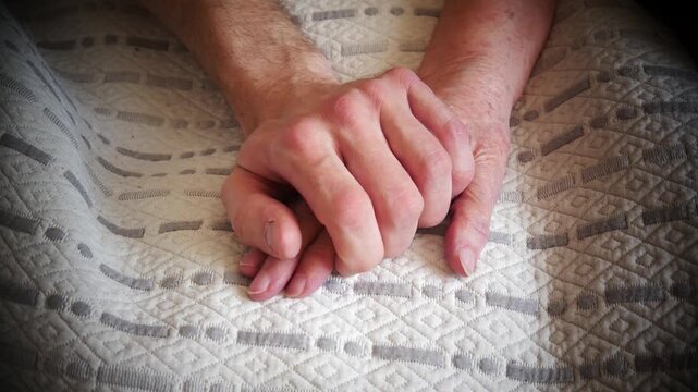 Close-up of a young man placing his hand on the hand of an elderly woman next to him