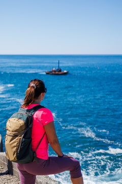 Female tourist with backpack looking at blue sea with floating fishing boat while hiking in Montenegro
