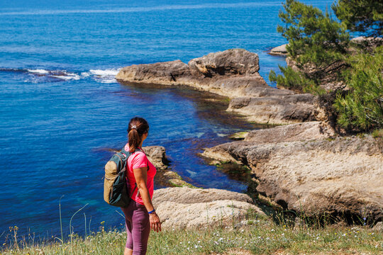 Woman tourist with backpack looking at blue sea while hiking on trekking trail along seashore in Montenegro