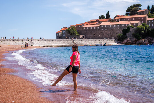 Mature woman walking and having fun on Sveti Stefan beach in Montenegro. Summer vacation in seaside resort