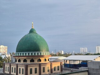 Beautiful green mosque dome with intricate patterns, set against an urban skyline under a clear sky, symbolizing harmony and cultural heritage. © auliyahanif
