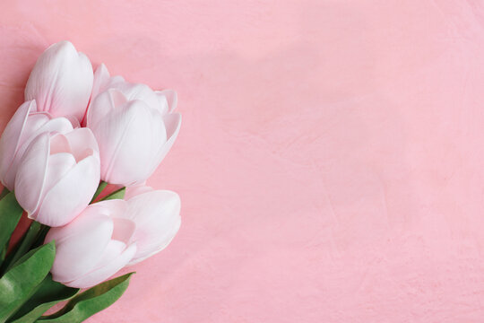 Beautiful soft pink tulips over pink textured homemade paper with copy space. Flatlay image for Mother's Day or other special occasions. 