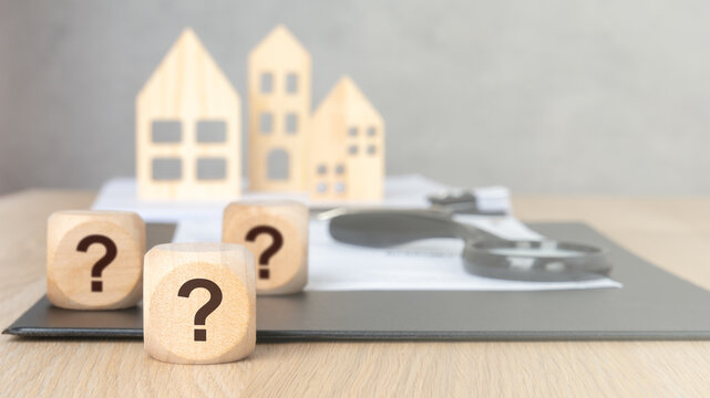 Wooden blocks with question marks magnifying glass and blurred house models.
