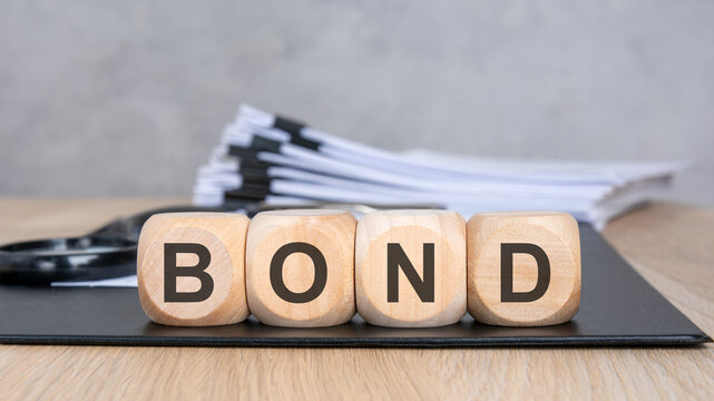 Wooden blocks with BOND text, blurred documents and magnifying glass.