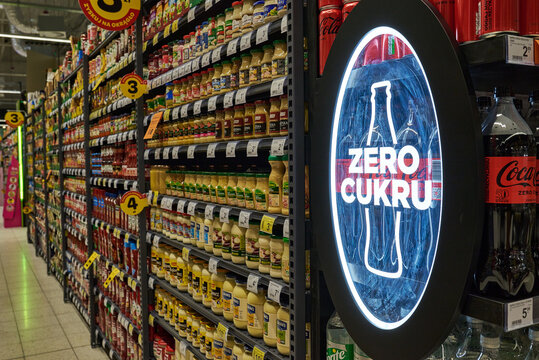 Supermarket aisle displaying various condiments, sauces, and mustard jars with a bright "Zero Cukru" sugar-free Coca-Cola sign