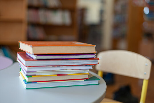 Colorful stack of hardcover books on round table in classroom or library interior. Back-to-school, study, reading and education.