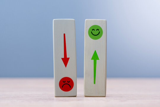 Wooden blocks featuring green happy face with up arrow and red sad face with down arrow on blue background. Concept service quality impact, reputation management and client feedback analysis.