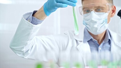Naklejka premium Scientist with protective gloves and glasses examining lab tube with a green fluid. Microbiology and science concept
