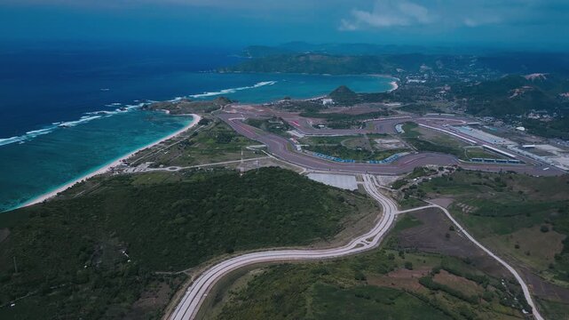 Aerial Coastal Highway Winding Toward Track Overlooking Azure Ocean, Curving Asphalt Corridors, Hillside Greenery, Construction Pads, Empty Intersection,Tanjung Aan,Kuta,Lombok,Indonesia