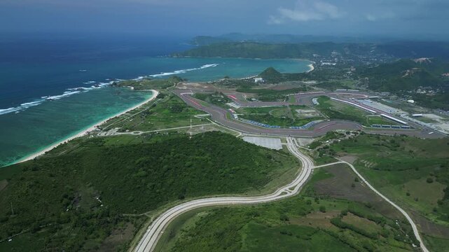 Aerial Coastal Highway Winding Toward Track Overlooking Azure Ocean, Curving Asphalt Corridors, Hillside Greenery, Construction Pads, Empty Intersection,Tanjung Aan,Kuta,Lombok,Indonesia