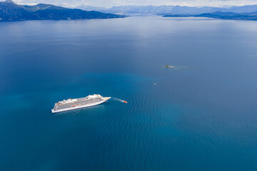 Obraz premium Stunning aerial view of a large luxury cruise ship sailing across the deep blue waters of the Ionian Sea near the coast of Corfu, Greece. Concept of summer vacation, travel, and maritime transport