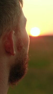 Free man pensively looks at setting sun. Tourist gazes into distance in nature. Portrait of man, close-up face. Happy man prays outdoors, sunrise, religion. Human journey. Man enjoys beautiful nature