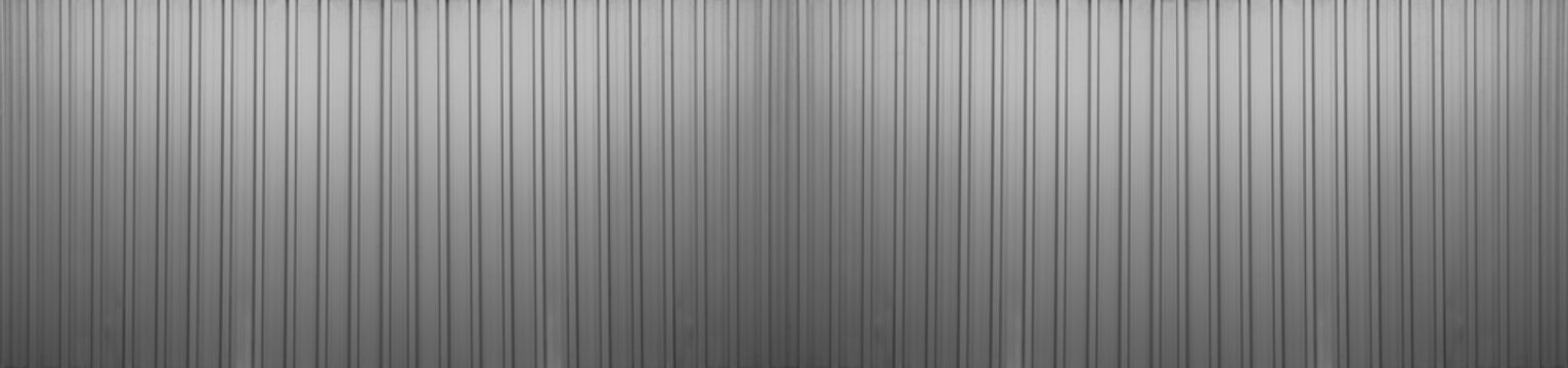 grey silver gray corrugated metal wall background texture with vertical lines and rivets. Clean industrial surface for construction or architectural backdrop. Frontal view with bright natural light.