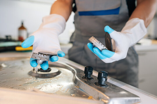 Close-up of professional cleaner hands in rubber gloves disassembling dirty gas hob for deep cleaning. Focus on appliance maintenance and domestic hygiene service. Bright, clean lighting.
