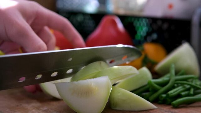 Home kitchen scene where a woman cuts pattypan squash with a big knife on a wooden board, while fresh tomatoes and green beans stand in the background, creating a warm and natural cooking moment.
