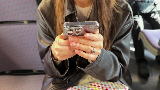 Young woman in black leather jacket using smartphone on public transport, female hands texting and scrolling social media on mobile phone, urban lifestyle commute, close up faceless shot indoors