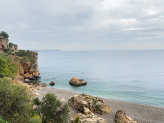 Naklejka premium Small rocky cove beach with cliffs on rainy cloudy day