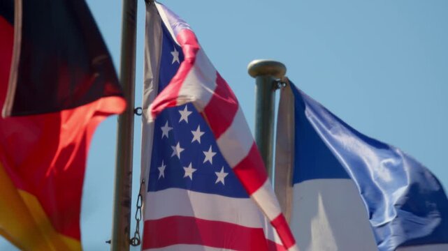 Cinematic shot of three national flags waving in the wind. Close up of American, German, and French flags against a clear blue sky, symbolizing international relations and western cooperation