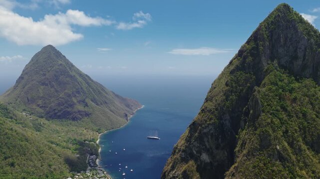 Stunning aerial view of iconic Pitons mountains in Saint Lucia rising dramatically from deep blue Caribbean waters, with lush green tropical vegetation, scattered white clouds.