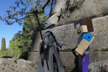 Obraz premium Minecraft figure of main character Steve meets action figure of wizard Gandalf from novel Hobit and Lord Of The Rings by J.R.R.Tolkien under ancient stone pedestal of lion statue, spring sunshine. 