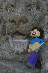 Obraz premium Action figure of main Minecraft Character Steve standing at open mouth of a giant lion statue in park.