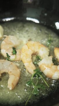 Vertical video. Preparing shrimp. Appetizer recipe. Prawn sizzling in pan with bubbling butter fresh herbs. Delicious gourmet food.