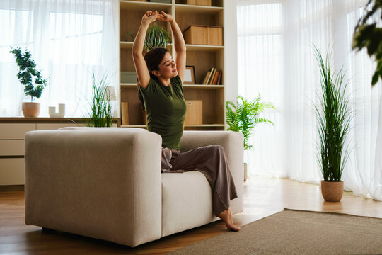 Woman stretching arms up, sitting comfortably in an armchair at home for relaxation