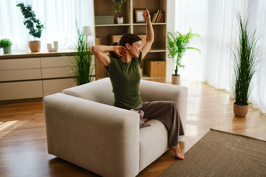 Woman waking up and stretching comfortably in an armchair at home during morning