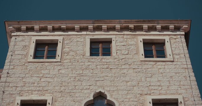 The upper section of a stone building facade with three rectangular windows and a roof cornice is shown on Square Tomaso Bembo.