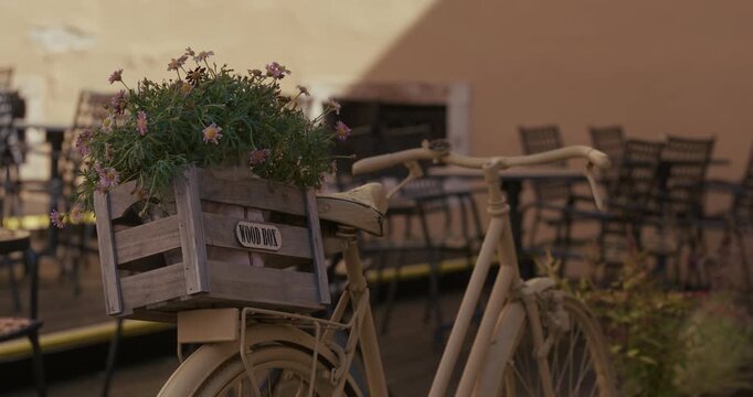 A bicycle with a wooden crate filled with flowers is parked beside outdoor tables and chairs.