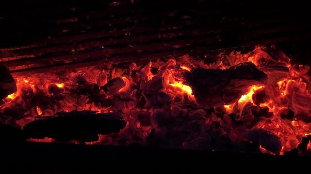 Glowing coals and dancing flames close-up outdoors. Burning coals with flickering flames, fiery texture close-up