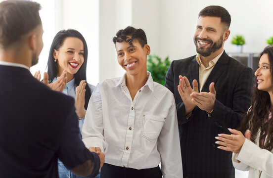 Happy diverse business team congratulating smiling female colleague, shaking hands and applauding in modern office. Employees celebrating achievement, showing support and appreciation for success.