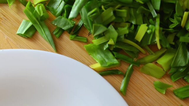 Chopped fresh wild leeks on wooden board. Organic asphodelus leaves prepared for healthy cooking in home kitchen setting.