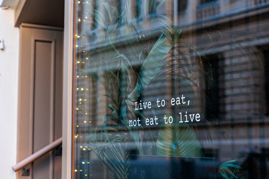 Live to Eat Sign On Cafe Window With Plants And Street Reflection
