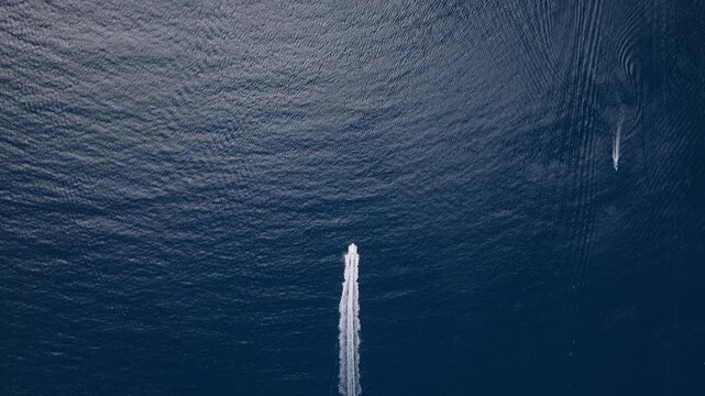 Drone footage captures two motorboats speeding across vast dark blue ocean waters leaving white foamy wake trails behind them. Birds eye view of nautical vessels on open sea.