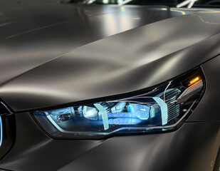 Obraz premium Front BI-LED headlight on a black matte car. Matte black premium car LED headlights close-up. Modern sport car headlight. BI-LED headlights of a modern and expensive black car, hood and radiator. 