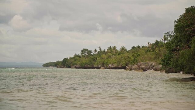 Wide rocky beach shoreline with sea and mangrove fringe under cloudy sky, gentle waves lapping shallow reef and distant horizon creating a calm cinematic atmosphere ideal for travel promos, coastal