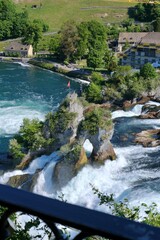 Obraz premium Rock formation in the middle of Rhine Falls with Swiss flag, surrounded by powerful flowing water and scenic natural landscape