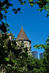 Naklejka premium Historic tower near Rhine Falls framed by green foliage against a deep blue summer sky in Switzerland
