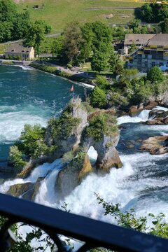 Rock formation in the middle of Rhine Falls with Swiss flag, surrounded by powerful flowing water and scenic natural landscape