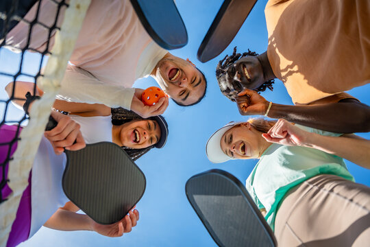 Diverse friends laughing huddle under pickleball net