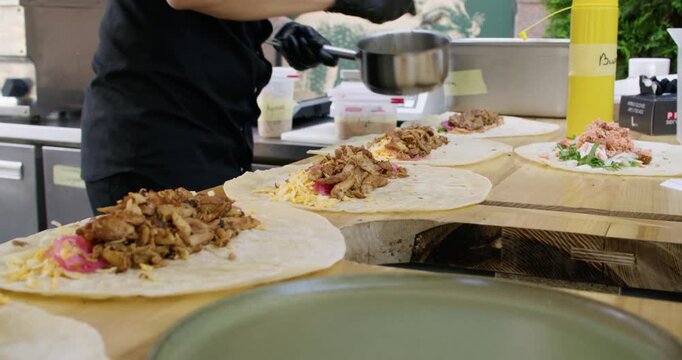 Cooking fast food. Kitchen process. Chef preparing appetizing chicken burrito placing meat cheese on flatbread tortillas on table.