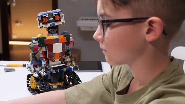 Young boy with glasses intently assembling a colorful robot from toy bricks, exploring stem skills, creativity and hands on learning at home during focused play and tinkering
