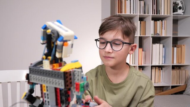 Young boy wearing glasses engaging in hands on stem learning activity by building a robot using a colorful plastic construction toy set at home, developing engineering skills