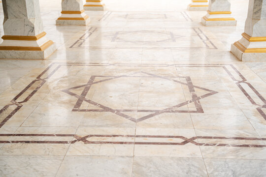 Mosque marble floor with geometric inlay pattern featuring eight pointed star motif between column bases in open courtyard. Islamic architecture, decorative flooring, exterior detail