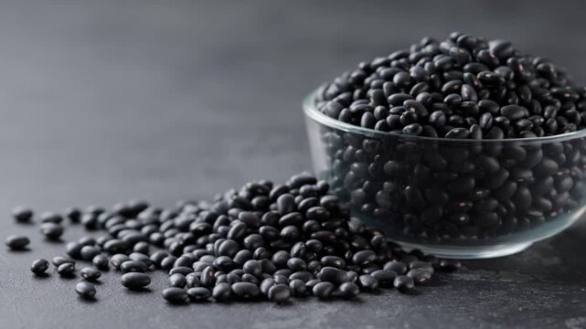 black beans in a glass plate and scattered on a dark stone table.