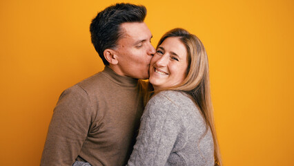 Fototapeta premium Happy couple showing love and affection, smiling while man kisses woman on cheek against an orange background