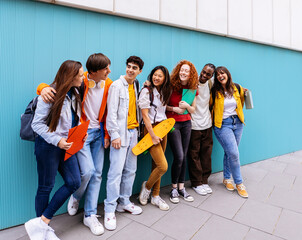 Fototapeta premium Young happy multiracial student friends standing over isolated blue background. Diverse teenage people having fun talking leaning on campus building college wall. Education and youth concept