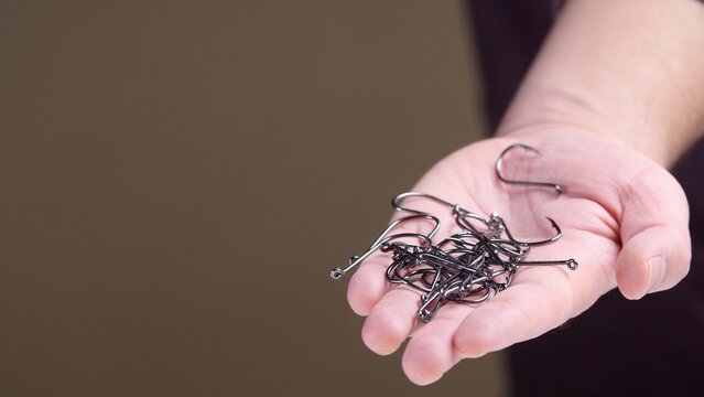 Hand holding a pile of sharp metal fishing hooks and tackle, close up detail of barbed steel gear for angling, freshwater or saltwater fishing, hobby or sport preparation