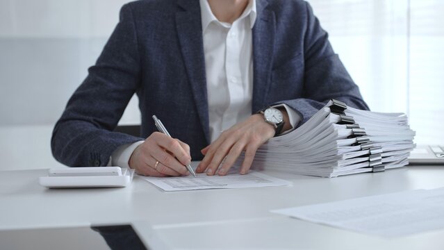 Business professional sorting a large stack of financial reports and tax forms with binder clips on a busy office desk. Audit and taxes